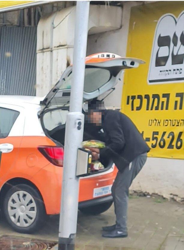 עובד העירייה מוציא אוכל מהרכב שחנה על המדרכה